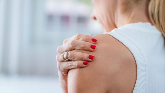 Kobieta trzymająca się za bolący bark, ilustrująca objawy zespołu bolesnego barku oraz problemy z ruchomością stawu ramiennego.