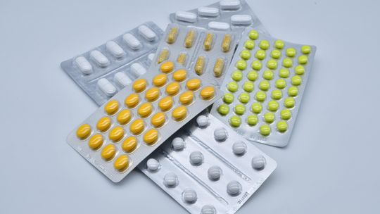 Blistry z różnymi tabletkami i kapsułkami leków na białym tle – ilustracja dotycząca farmaceutyków, leczenia i ochrony zdrowia.