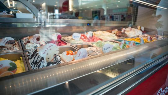 Witryna lodziarni wypełniona różnymi smakami lodów, opisanymi etykietami i ułożonymi w metalowych pojemnikach za szklaną ladą. Ujęcie dobrze oddaje znaczenie sprawnego zaopatrzenia lodziarni w sezonie, gdy liczy się dostępność smaków i dodatków.