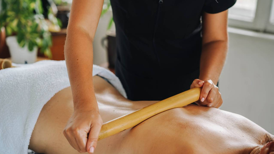 Masaż antycellulitowy maderoterapia wykonywany drewnianym wałkiem na plecach pacjentki w gabinecie PerfectLook Clinic.