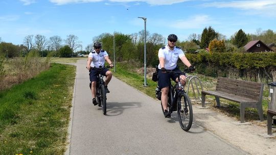 Policyjny patrol rowerowy podczas służby na ulicach Zamościa. Funkcjonariusze na elektrycznych rowerach patrolują ścieżki rowerowe i miejsca rekreacji w mieście.