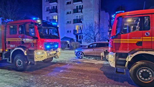 Dwa wozy strażackie w nocy zaparkowane przed blokiem