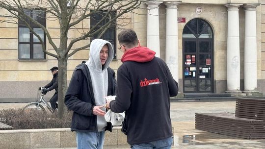 Dziennikarz Dziennika Wschodniego z torebkami wypełnionymi pączkami wręcza drugiemu mężczyźnie paczkę z pączkiem