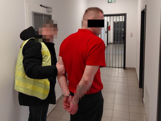 Kradzież kasy, policyjny pościg i alkohol. 31-latek z powiatu ryckiego trafił do aresztu Podejrzany w kajdankach prowadzony przez funkcjonariusza policji