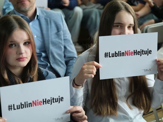 Dwie nastolatki siedzące na sali trzymają kartki z napisem „#LublinNieHejtuje” podczas inauguracji kampanii społecznej przeciw hejtowi