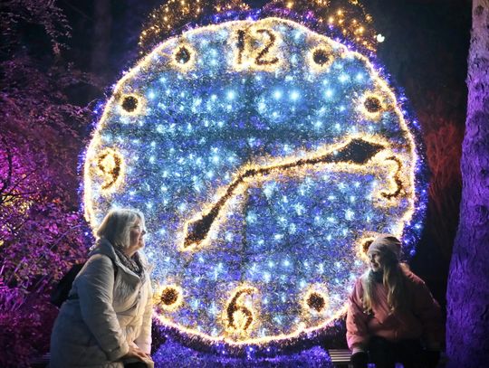 Świetlna instalacja w kształcie zegara w Lumina Parku w Lublinie – dwie osoby pozują na tle iluminacji nocą.