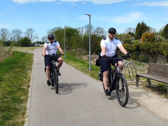 Policyjny patrol rowerowy podczas służby na ulicach Zamościa. Funkcjonariusze na elektrycznych rowerach patrolują ścieżki rowerowe i miejsca rekreacji w mieście.