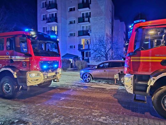 Dwa wozy strażackie w nocy zaparkowane przed blokiem