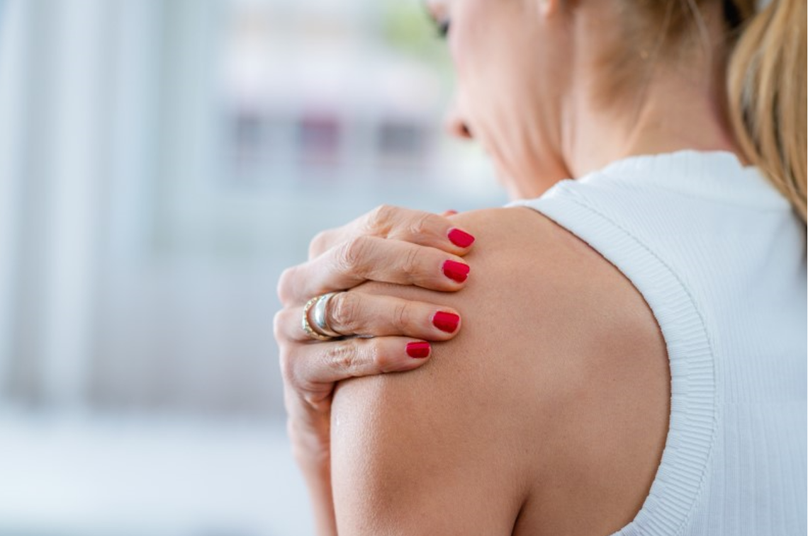 Kobieta trzymająca się za bolący bark, ilustrująca objawy zespołu bolesnego barku oraz problemy z ruchomością stawu ramiennego.