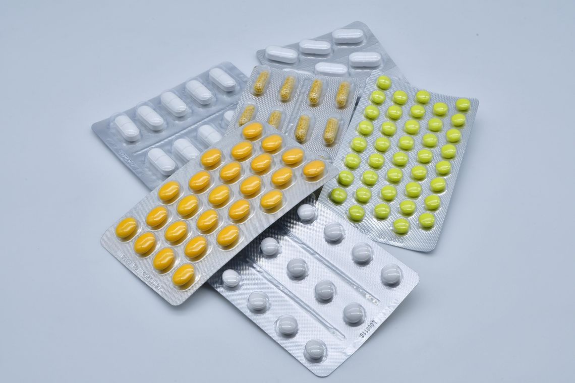 Blistry z różnymi tabletkami i kapsułkami leków na białym tle – ilustracja dotycząca farmaceutyków, leczenia i ochrony zdrowia.