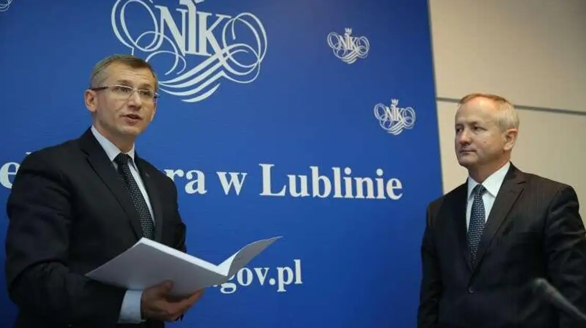 Dwaj przedstawiciele Najwyższej Izby Kontroli (NIK) podczas konferencji prasowej w Lublinie na tle niebieskiej ścianki z logo instytucji.