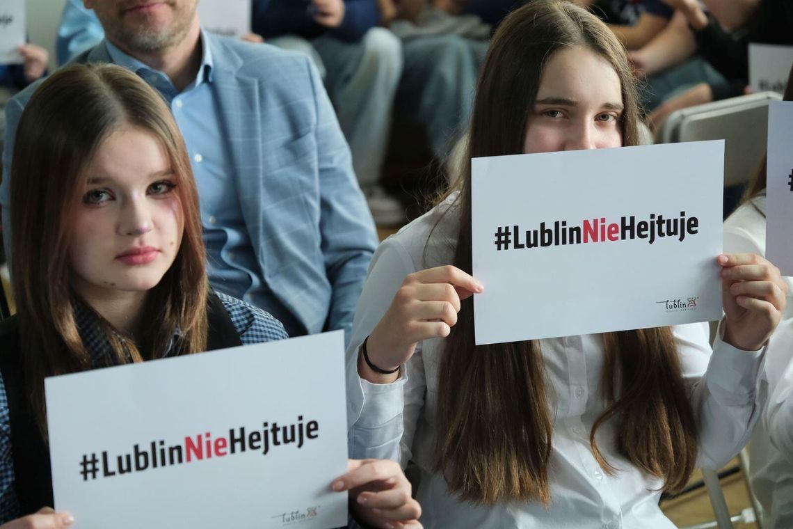 Dwie nastolatki siedzące na sali trzymają kartki z napisem „#LublinNieHejtuje” podczas inauguracji kampanii społecznej przeciw hejtowi