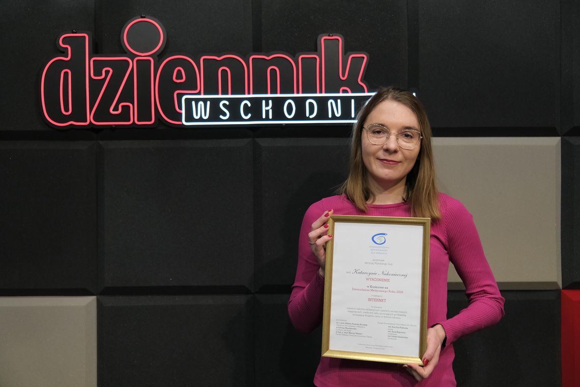 Dziennikarka z dyplomem na tle neonu Dziennika Wschodniego