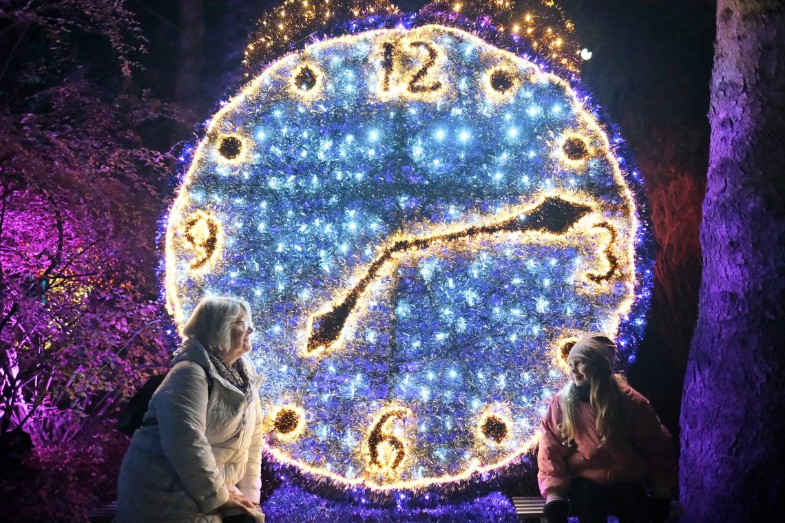 Ostatni dzwonek by wskoczyć do Krainy Czarów. Lumina Park w Lublinie żegna się z feriami Świetlna instalacja w kształcie zegara w Lumina Parku w Lublinie – dwie osoby pozują na tle iluminacji nocą.