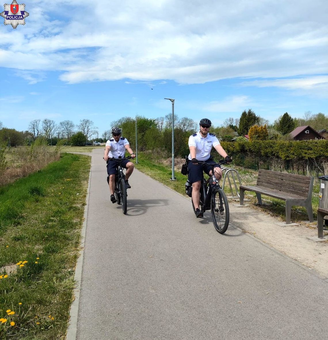 Policyjny patrol rowerowy podczas służby na ulicach Zamościa. Funkcjonariusze na elektrycznych rowerach patrolują ścieżki rowerowe i miejsca rekreacji w mieście.