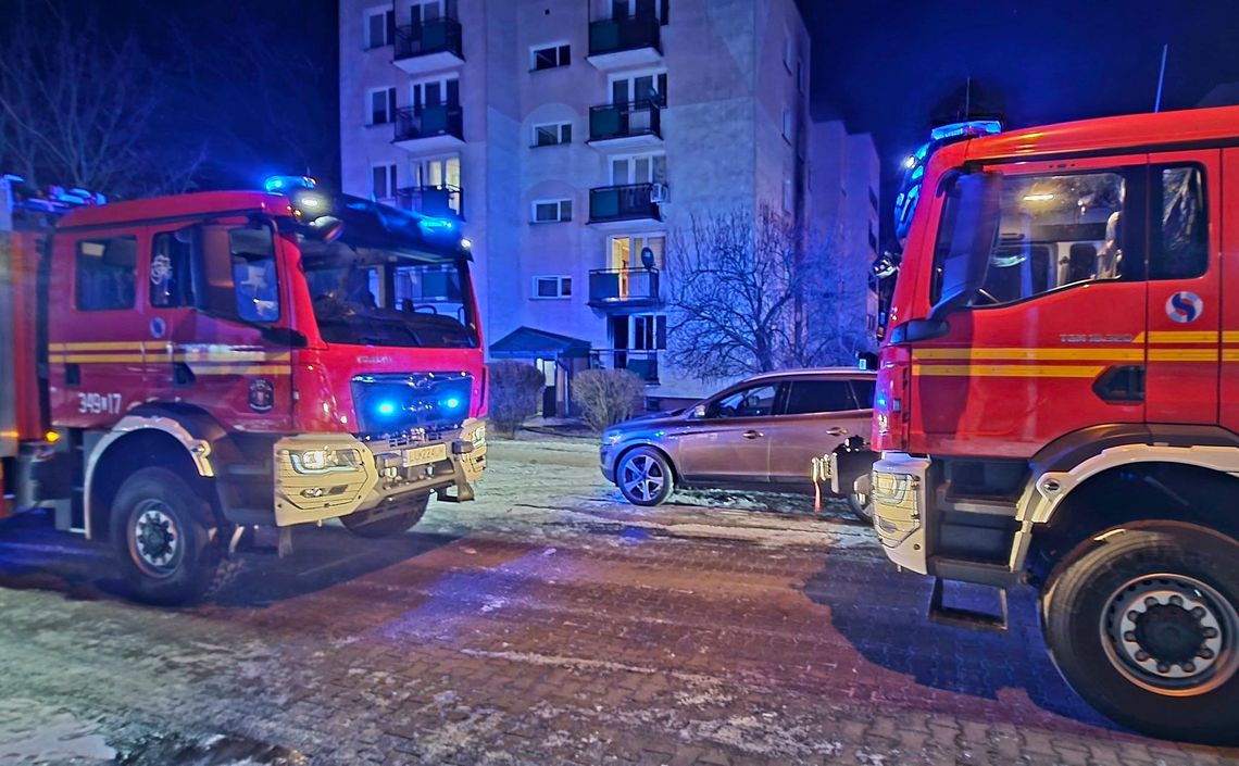 Dwa wozy strażackie w nocy zaparkowane przed blokiem