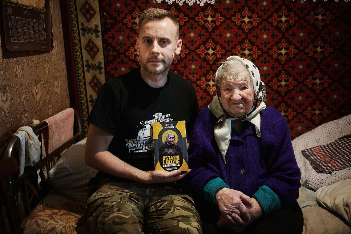 Mężczyzna i starsza kobieta siedzą w domu, prezentując książkę „Ostatni ludzie Czarnobyla” o mieszkańcach strefy wykluczenia.