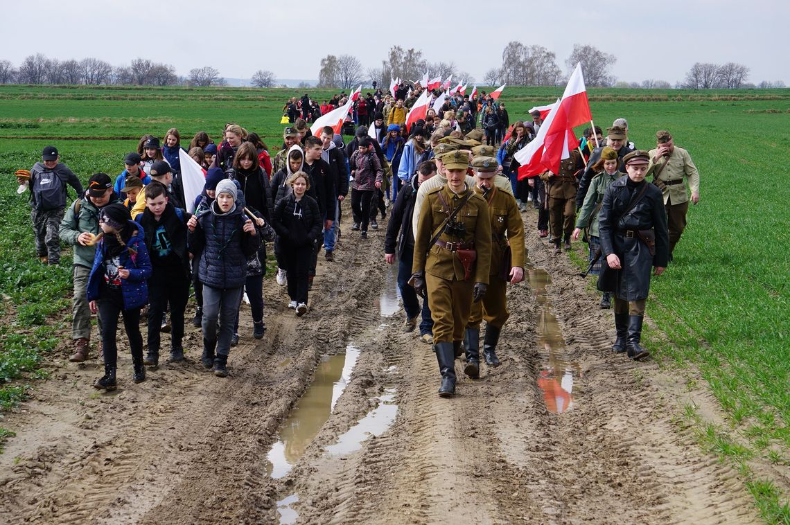 Śladami pamięci żołnierzy AK i WiN — rajd pieszy w Bełżycach Uczestnicy marszu patriotycznego z biało-czerwonymi flagami idą polną drogą podczas historycznego wydarzenia na Lubelszczyźnie.
